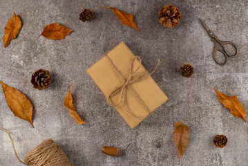 Gift box with autumn leaves,cones,acorns, scissors, twine on a gray background. Flat lay, top view.