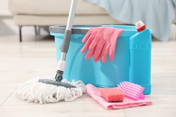 String mop and bucket with cleaning supplies on wooden floor indoors