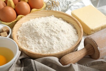 Rolling pin and ingredients for dough on table, closeup