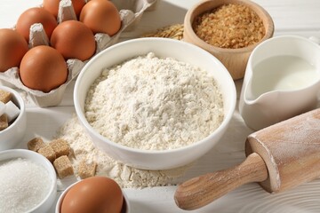 Rolling pin and ingredients for dough on white wooden table, closeup
