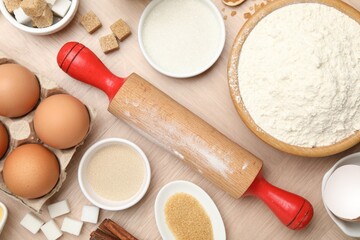 Rolling pin and different ingredients on wooden table, flat lay