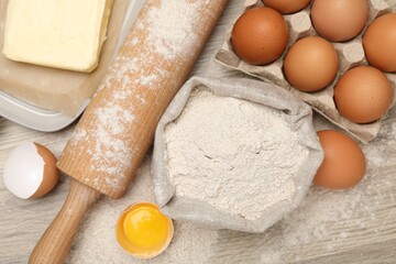 Rolling pin and different ingredients on light wooden table, flat lay