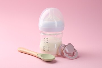 Feeding bottle with milk, spoon and pacifier on pink background