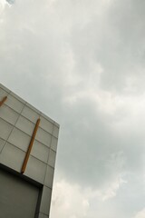 A minimalist modern building facade with geometric design and yellow accents against a cloudy sky. Captured from a low-angle perspective.