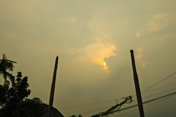 A dramatic sunset partially hidden by clouds, casting a golden glow over the sky. Silhouettes of...