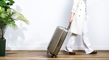 Beige plastic suitcase on wheels in woman hands in white trench coat and trousers and casual...