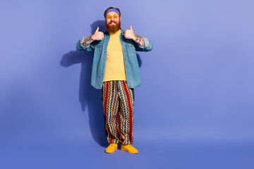 Fototapeta premium Stylish man with a beard in vibrant attire giving thumbs up against a purple background