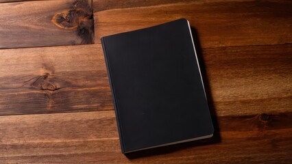 Black notebook mockup on a wooden table, perfect for design and branding projects.
