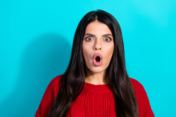 Surprised stylish young brunette woman in a red knitted sweater against a vibrant turquoise...