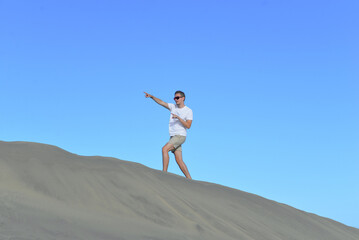 A young man walking along a sand dune through barkhan in Maspalomas, Gran Canaria on a hot sunny day. A self confident man goes up the mountain - success and achievements concept