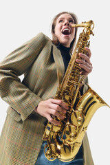 Emotional and joyful young woman, saxophone player in stylish blazer playing with energy against...