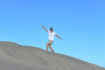 A young man walking along a sand dune through barkhan in Maspalomas, Gran Canaria on a hot sunny day. A self confident man goes up the mountain - success and achievements concept