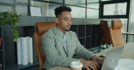 A focused businessman working on a laptop in a modern office, surrounded by charts and a coffee cup, emphasizing productivity and professionalism.