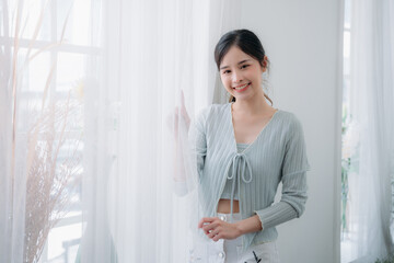 Young woman is standing and hands together in the shape of a heart in a room.