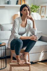 Beautiful woman posing looking at camera while sitting on stool in the living room at home
