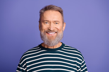 Obraz premium Cheerful mature man with grey beard smiling in striped shirt against purple studio background