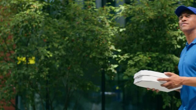 African American delivery man guy male courier in uniform pizzeria cafe worker walking in city outdoors urban going to client address buyer carrying pizza boxes packages profession small business