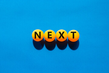 Next symbol. Concept word Next on beautiful yellow ping pong balls. Beautiful blue table blue...