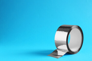 Roll of silver adhesive tape on light blue background, space for text