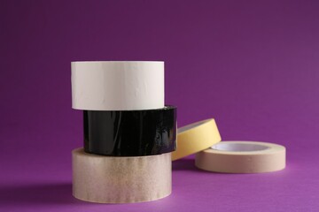 Rolls of different adhesive tapes on purple background