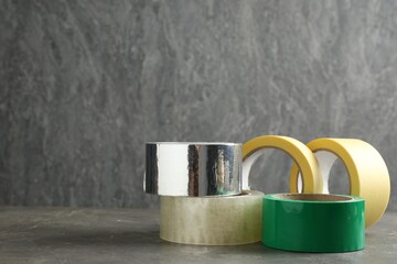Rolls of different adhesive tapes on grey table, space for text