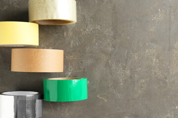 Rolls of different adhesive tapes on grey table, flat lay. Space for text