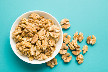 Top view of shelled walnuts into bowl on blue background.