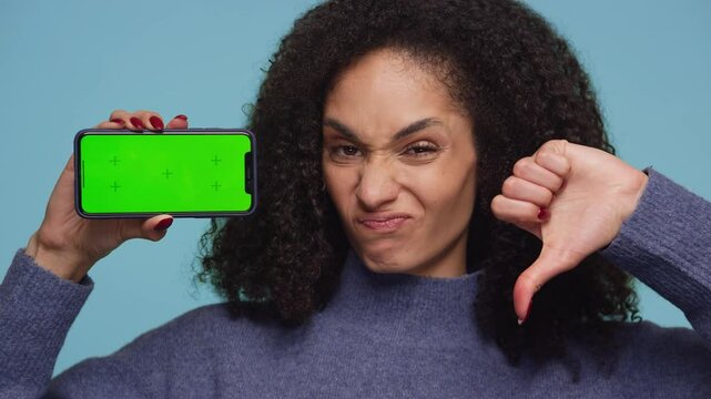Displeased Woman Holding Smartphone with Thumbs Down on Blue Background