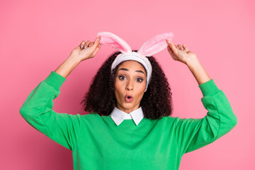Playful young woman with bunny ears in green pullover posing with charming expressions against pink...