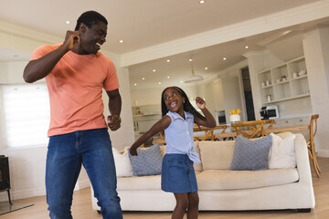 African American father and daughter dancing joyfully in living room, sharing playful moment