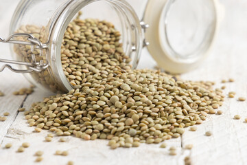 Fototapeta premium Glass jar full of dried raw green lentils on white table closeup. Traditional mediterranean legume