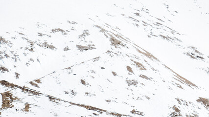 Aerial view of snowy mountain terrain. Snow completely covers the ground. Ideal for texture, pattern and background.