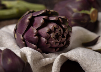 Heads of purple raw romanesco artichokes on napkin on dark table closeup. Fresh italian vegetables