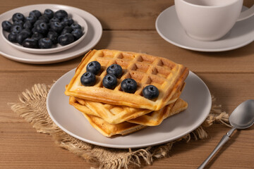 Delicious homemade waffles served with fresh blueberries on a wooden table in the morning
