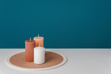 Brown, white and beige unlit candles stand on a round woven napkin on a blue background. Horizontal interior photo. Copy space