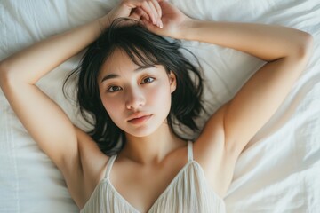 Naklejka premium A Japanese woman lies on a white bed, with her hands placed under her head.