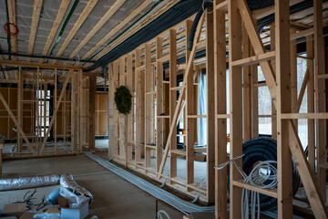 Wooden framing, exposed ventilation ducts, and wiring inside a house under construction. Large...