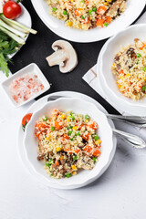 Couscous is a dish made from wheat grains (semolina) or millet. Lean couscous with mushrooms, corn, peas, herbs, tomatoes. Top view. Flatlay. Couscous on a light background.