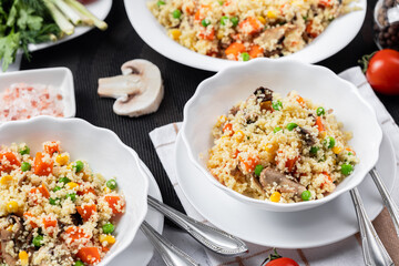Couscous is a dish made from wheat grains (semolina) or millet. Lean couscous with mushrooms, corn, peas, herbs, tomatoes. Side view. Flatlay. Couscous on a light background. Couscous in a white plate
