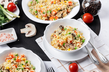 Couscous is a dish made from wheat grains (semolina) or millet. Lean couscous with mushrooms, corn, peas, herbs, tomatoes. Side view. Flatlay. Couscous on a light background. Couscous in a white plate