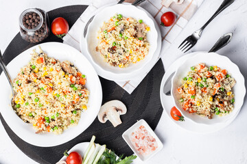 Couscous is a dish made from wheat grains (semolina) or millet. Lean couscous with mushrooms, corn, peas, herbs, tomatoes. Top view. Flatlay. Couscous on a light background.