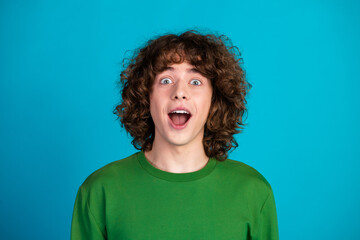 Young man in green sweatshirt with surprised expression on blue background, showcasing youthful...