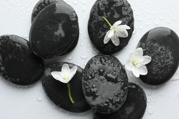 Wet spa stones and beautiful flowers on white background, flat lay