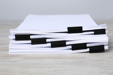 Binder clips with sheets of paper on wooden table, closeup