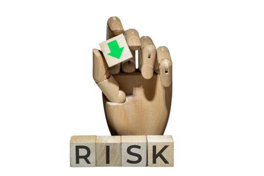 sztuczna ręka trzymająca kostkę z zieloną strzałką w dół nad napisem na kostkach: RISK. Koncepcja zarządzania ryzykiem.
