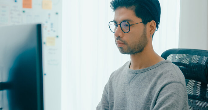 Young adult Asia male freelance eyeglasses typing write prompt AI bot IT app smart program nomad, video game, terminal with coding, user interface, designer, big data center on desktop computer.