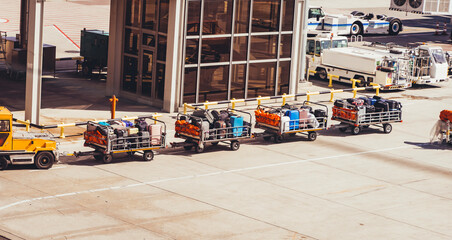 Airport baggage carts loaded with suitcases being transported on the tarmac. Ground handling operations, logistics, and airline travel infrastructure in bright daylight.