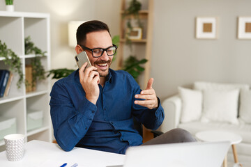 Smiling businessman making a phone call and gesturing while working remotely from his home office