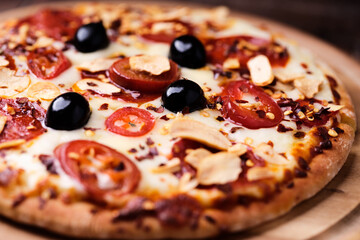 Pizza with salami and mozzarella cheese, jalapeno pepper and black olives. Wooden background. Soft focus. Close up.	