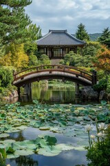 Japanese garden with wooden bridge crossing water lily pond leading to traditional building surrounded by green trees and hills under cloudy sky.